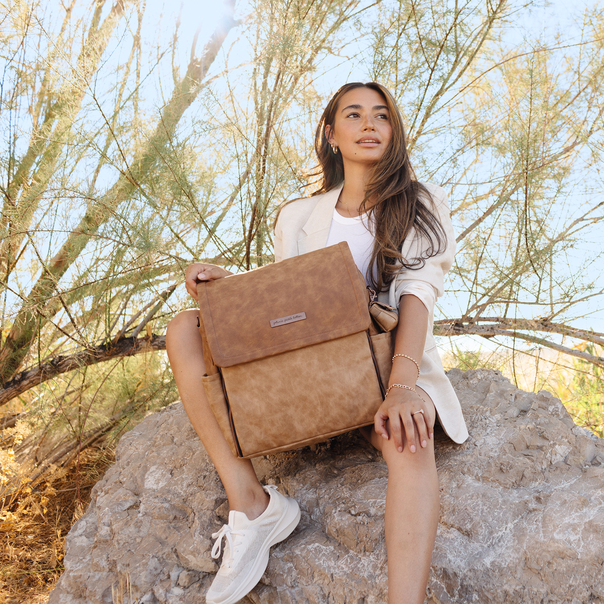 mom sitting on rock while holding the boxy backpack in brioche