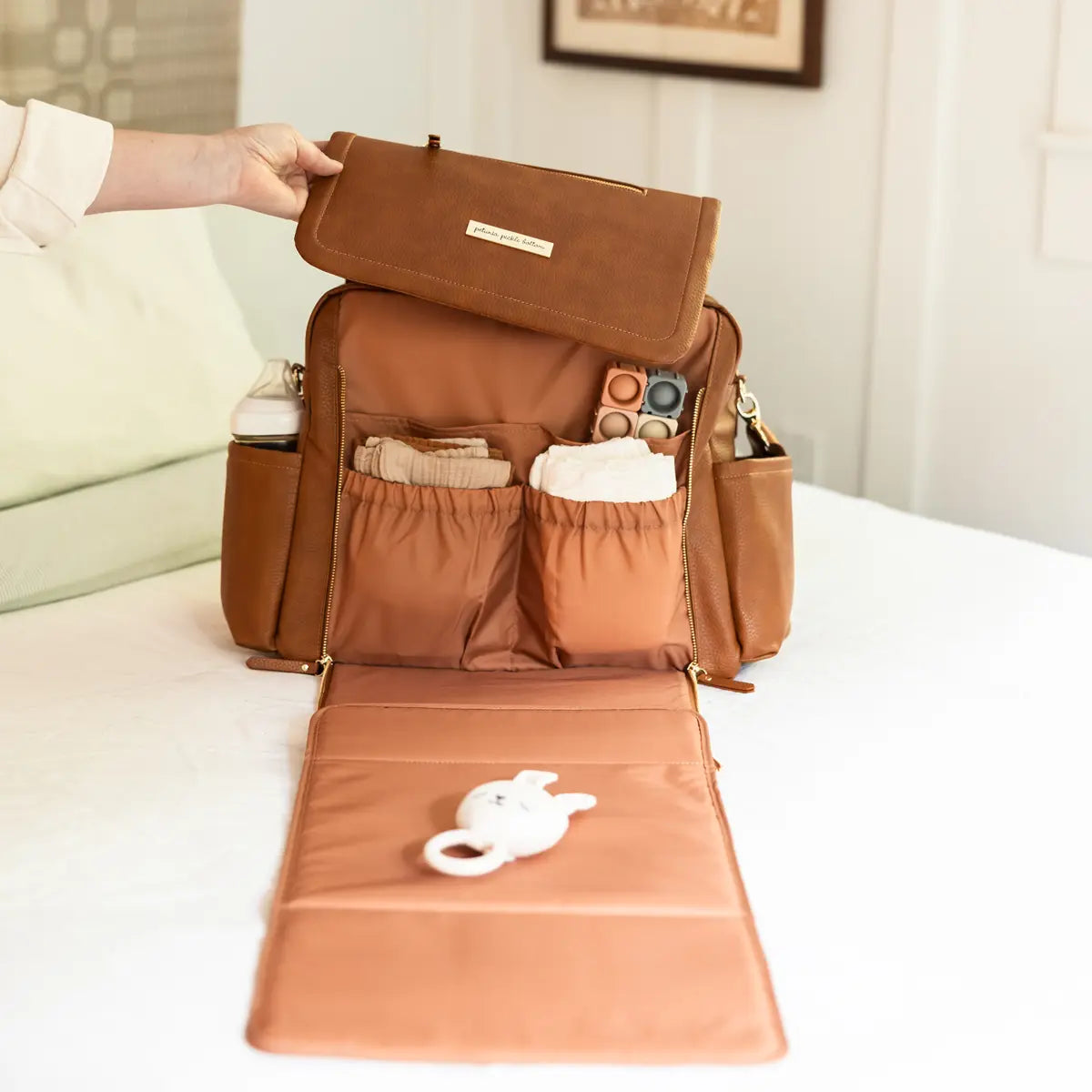 Open brown diaper backpack with organized interior pockets and fold-out changing pad displayed on a bed.