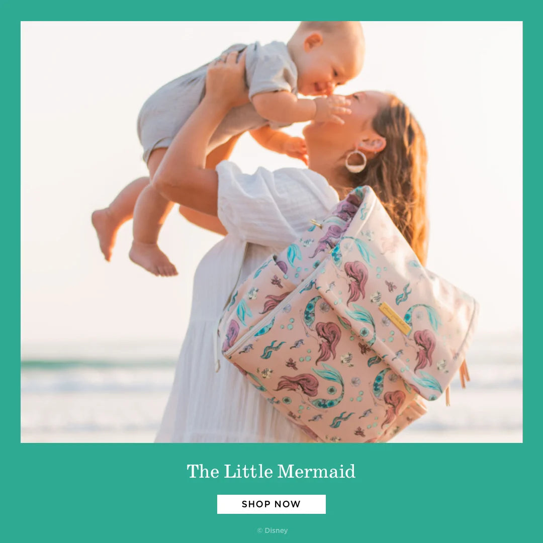the little mermaid. shop now. by disney. mom wearing the boxy backpack in little mermaid while holding baby