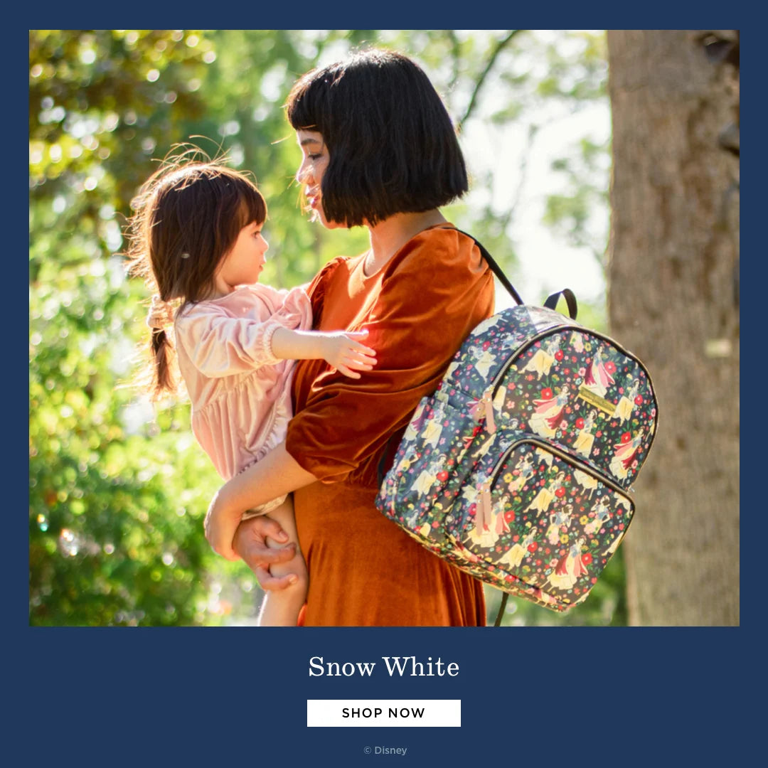 snow white. shop now. by disney. mom wearing the district backpack in snow white's enchanted forest while holding baby girl.