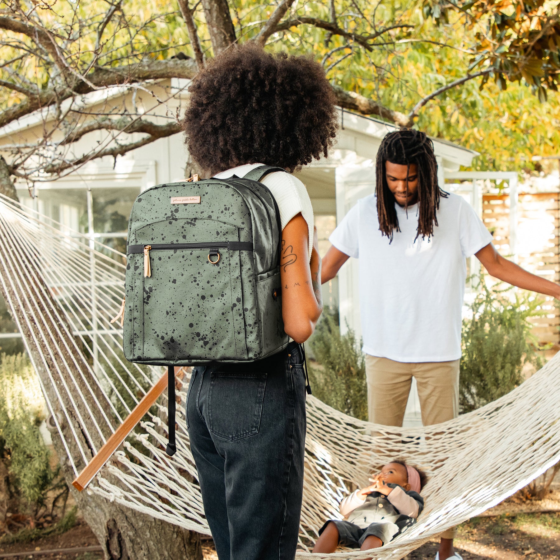 Outdoor scene featuring family at hammock with mom wearing green & black printed diaper bag backpack