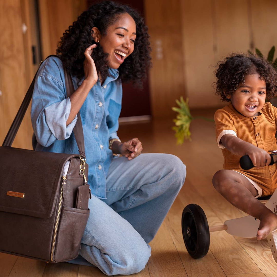 mom watching baby play on wooden kid's bike with the Boxy Backpack in Saddle over her shoulder