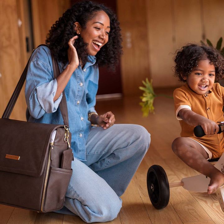 mom watching baby play on wooden kid's bike with the Boxy Backpack in Saddle over her shoulder