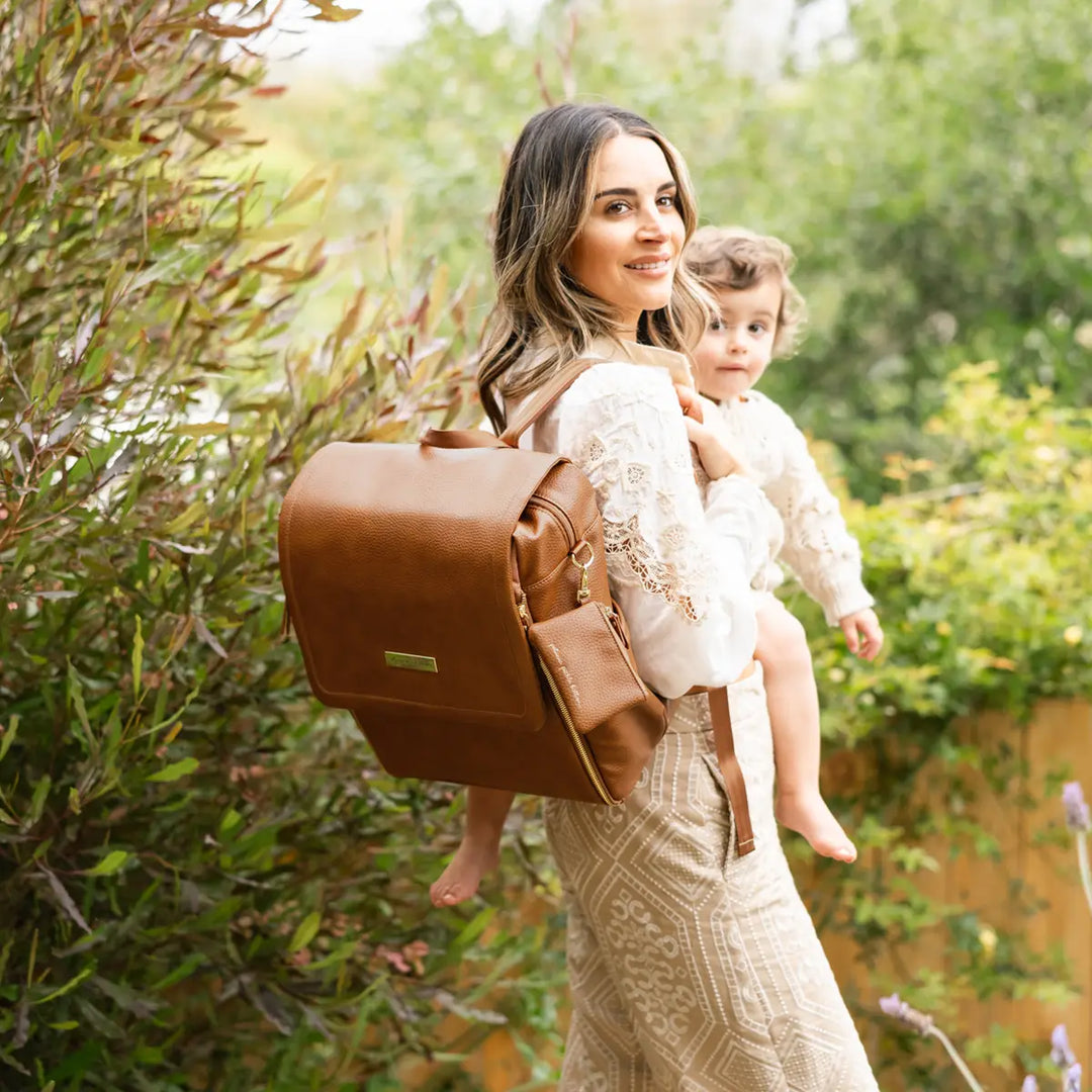 mom holding baby while wearing the boxy backpack in cedar