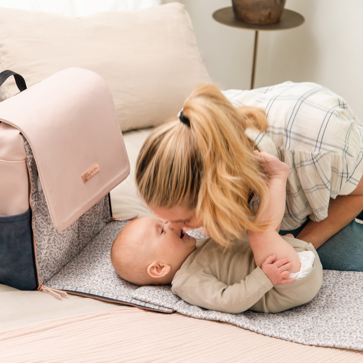 mom playing with baby while baby lies down on the diaper changing pad of the boxy backpack in indigo blush
