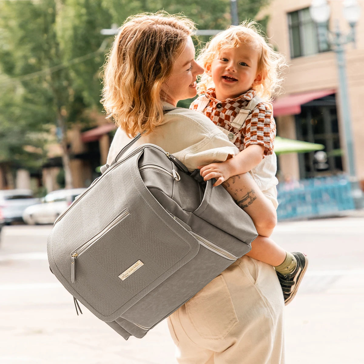 mom wearing the boxy backpack deluxe in sand cable stitch while holding baby