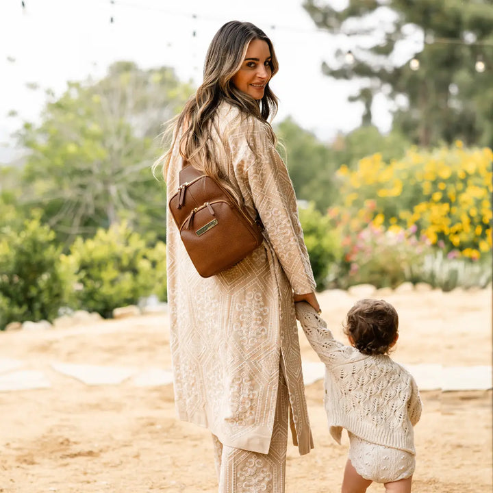 mom wearing the criss-cross sling in cedar while holding hands with baby