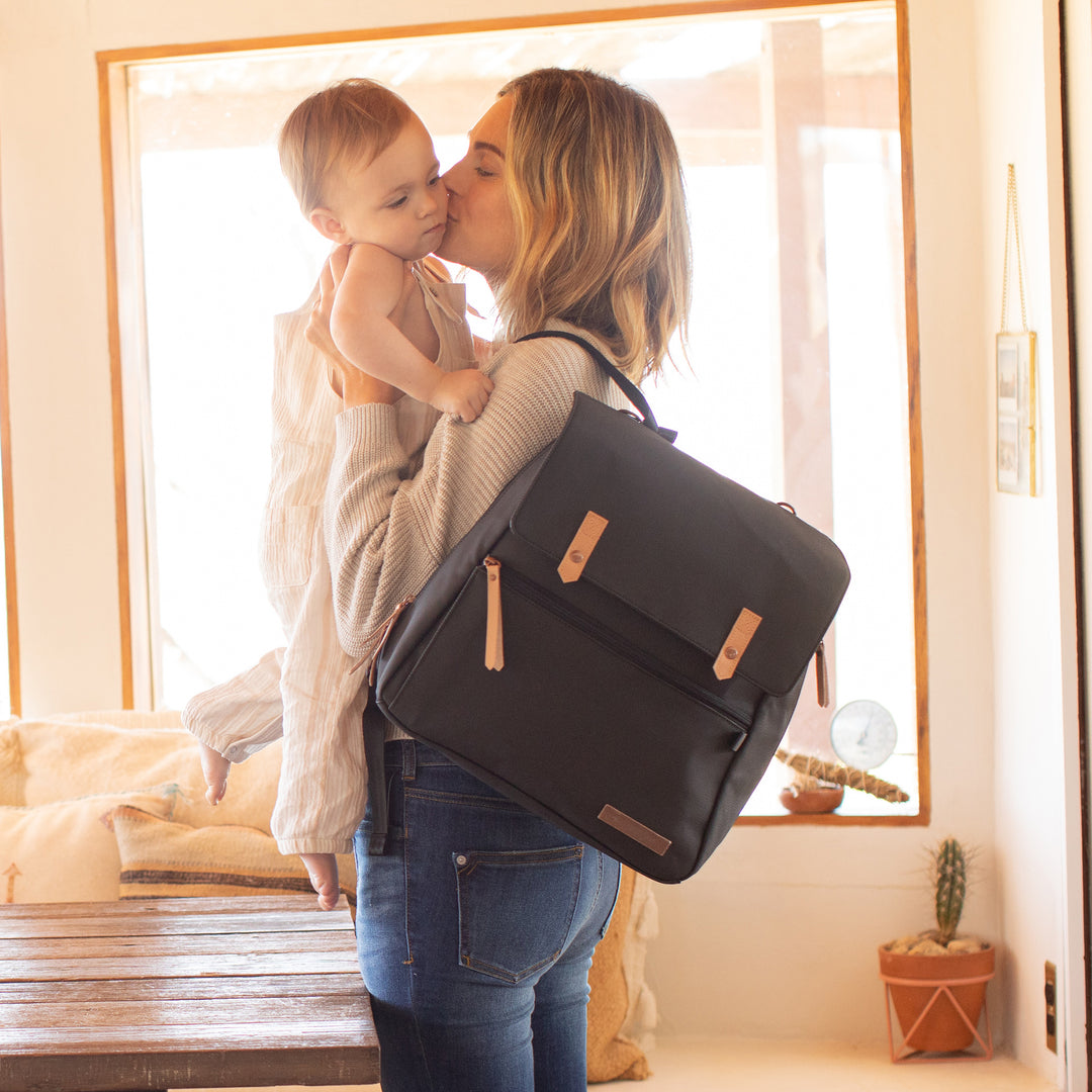 mom wearing meta backpack in black matte leatherette while holding and kissing baby