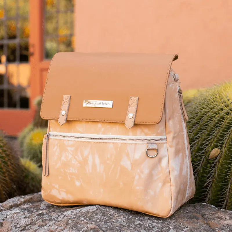 Meta Backpack in Dusted Desert Tie Dye. A soft caramel bag that is neutral and timeless shown on a rock with cacti in the background.