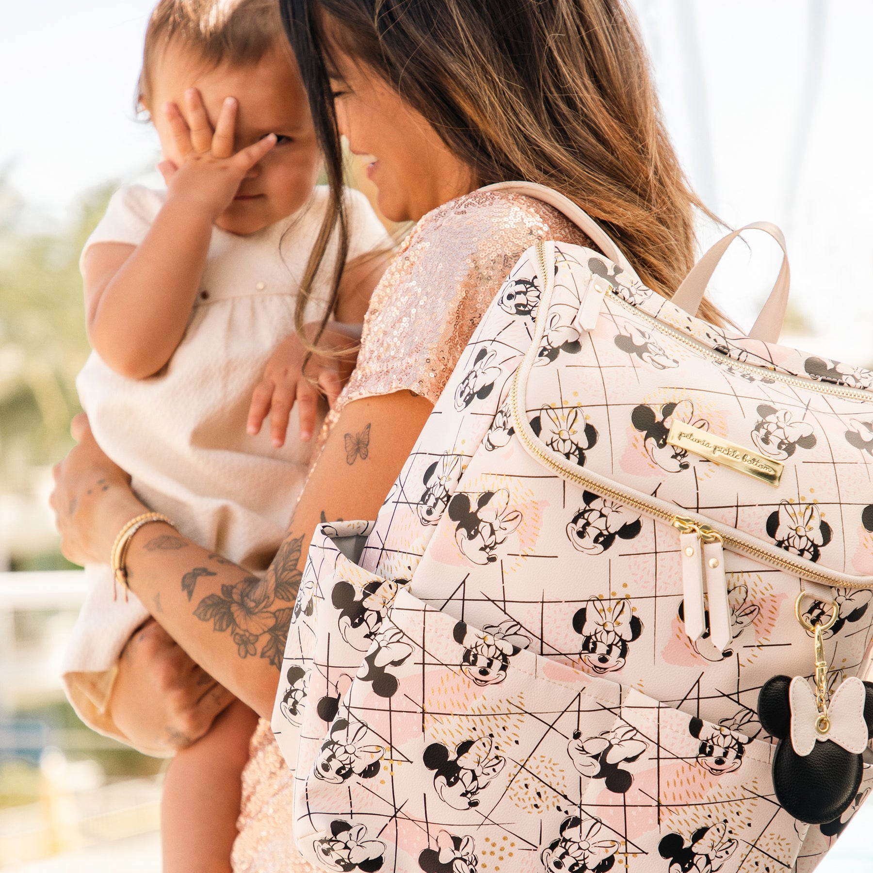 mom holding baby in her arms while wearing the method backpack in shimmery minnie mouse