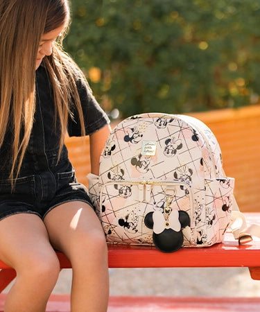 girl sitting on bench next to mini backpack in shimmery minnie