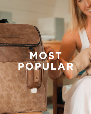 Most Popular. Mom holding baby while having the Tempo Backpack in Brioche displayed on table.