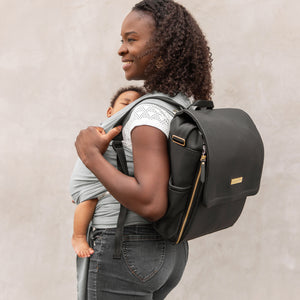 mom wearing boxy backpack in matte black while wearing infant son in baby wrap