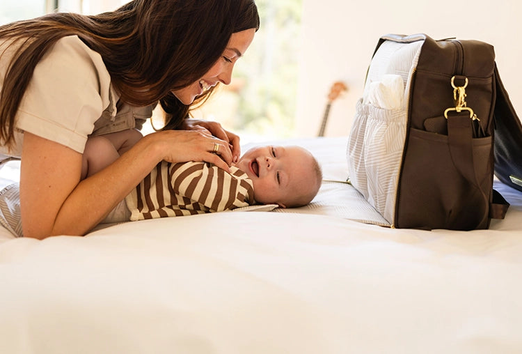mom playing with baby while baby lies on the diaper changing pad of the boxy backpack in saddle