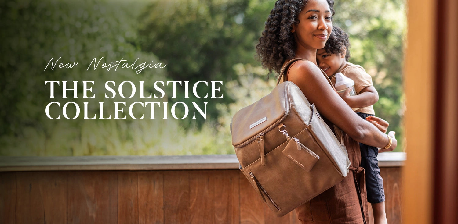 new nostalgia the solstice collection. mom wearing the tempo backpack in mink, holding toddler son