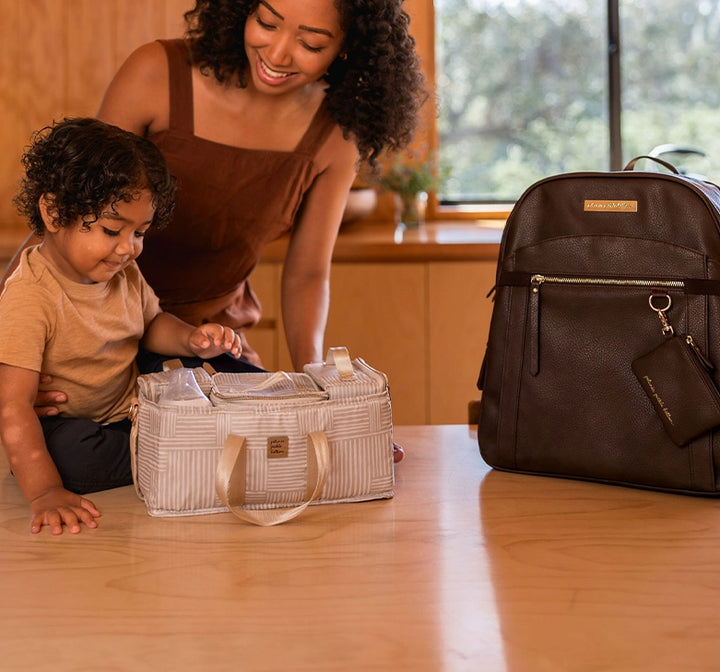 mom playing with baby displaying the inter-mix deluxe kit in checker stitch and provisions backpack in saddle