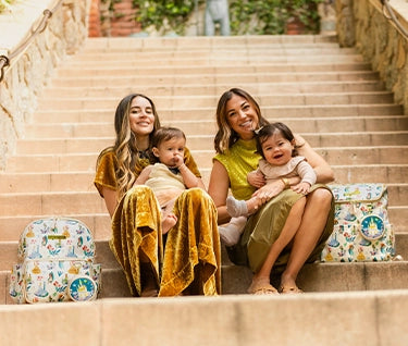 2 moms and 2 babies on the stairs next to the method and district backpack in disney princess courage and kindness