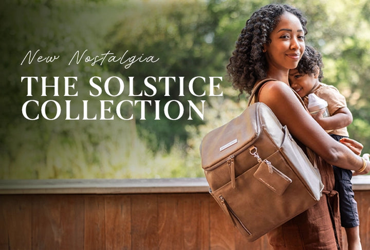 new nostalgia the solstice collection. mom wearing the tempo backpack in mink, holding toddler son