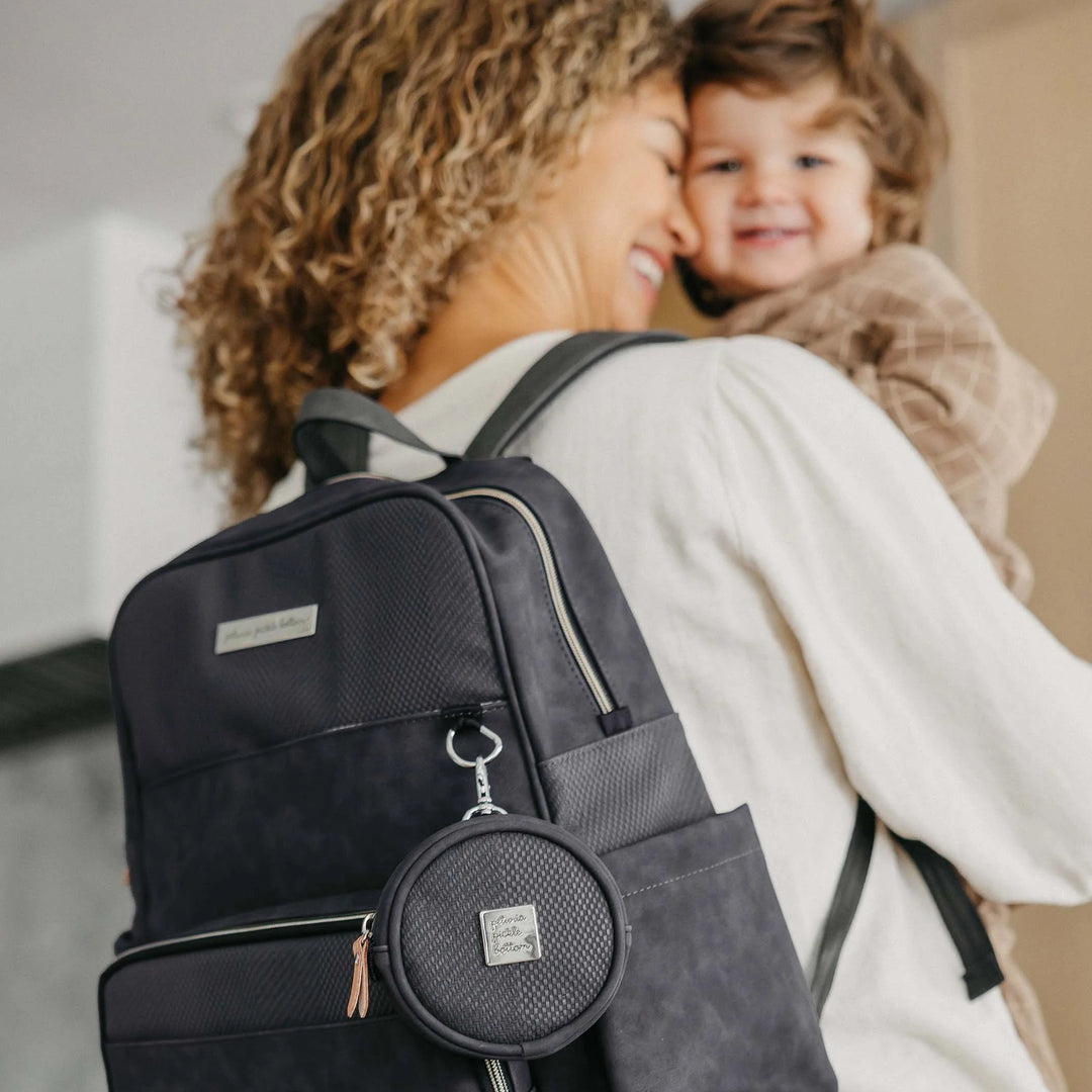 mom hugging baby while wearing the sync backpack in carbon cable stitch