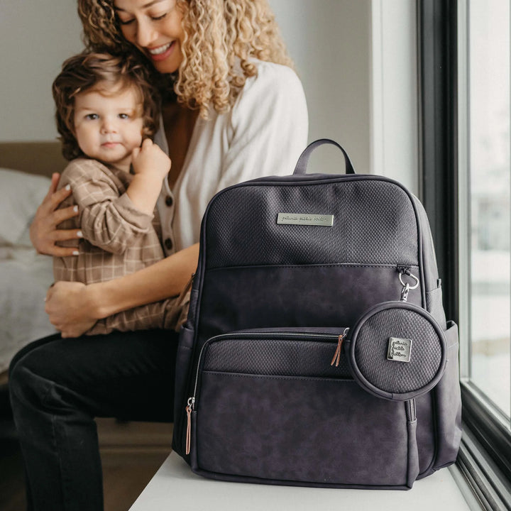 mom hugging baby while displaying the sync backpack and petite porter in carbon cable stitch