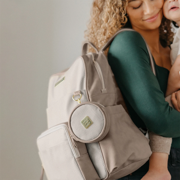 mom carrying baby. petite porter in grey matte cable stitch is attached to d ring of sync backpack in grey matte cable stitch. 