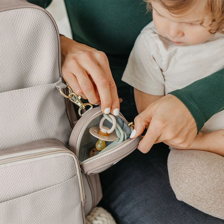 mom holding baby while putting inside pacifier inside the petite porter in grey matte cable stitch