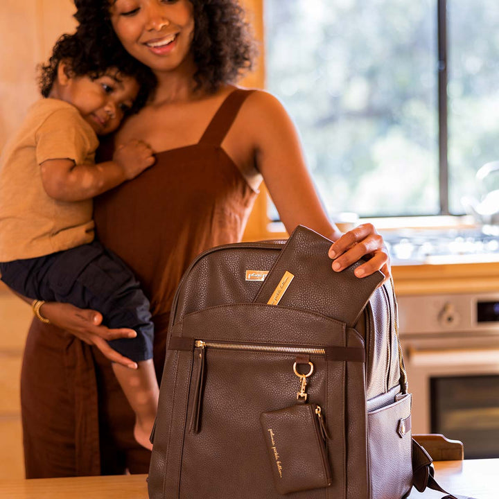 mom holding baby while putting organizer pouch in the 2-in-1 Provisions Breast Pump & Diaper Bag Backpack in Saddle