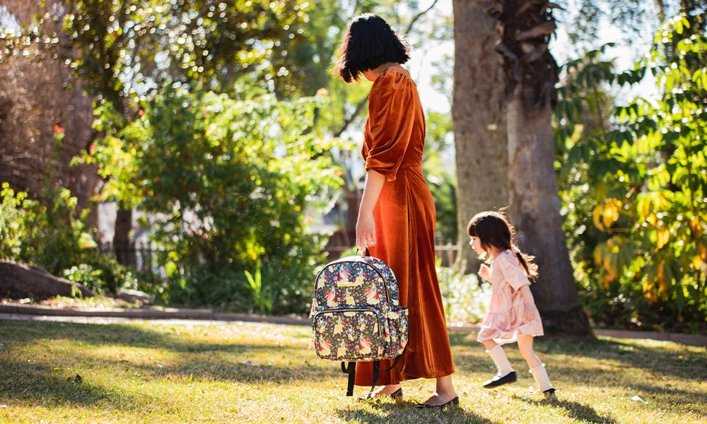 mom and baby walking in the sunny forest while mom is holding the district backpack in disney's snow white's enchanted forest