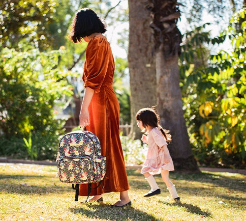 mom and baby walking in the sunny forest while mom is holding the district backpack in disney's snow white's enchanted forest