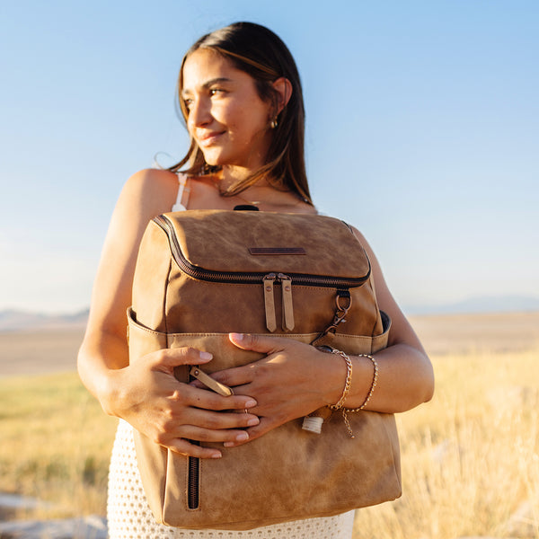 tempo backpack diaper bag in luxe faux vegan leather shown in supple two tone brown held by mom