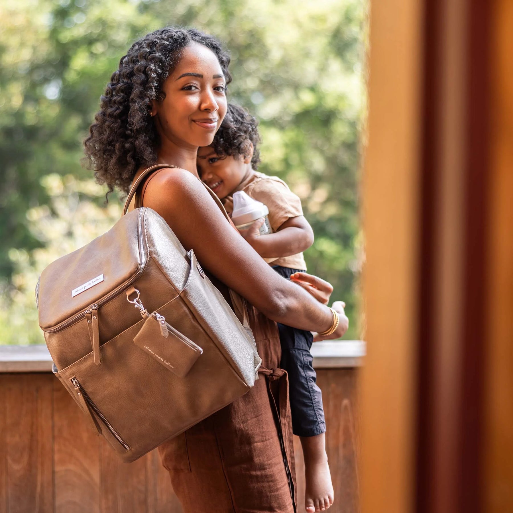 mom holding baby while wearing the tempo backpack in mink over her shoulder