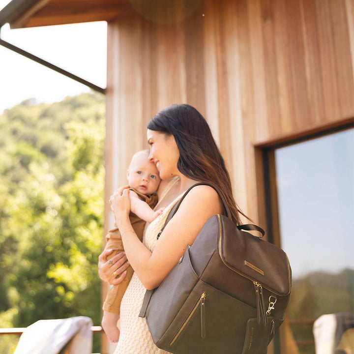 mom hugging and holding baby with the Tempo Backpack in Saddle over her shoulder