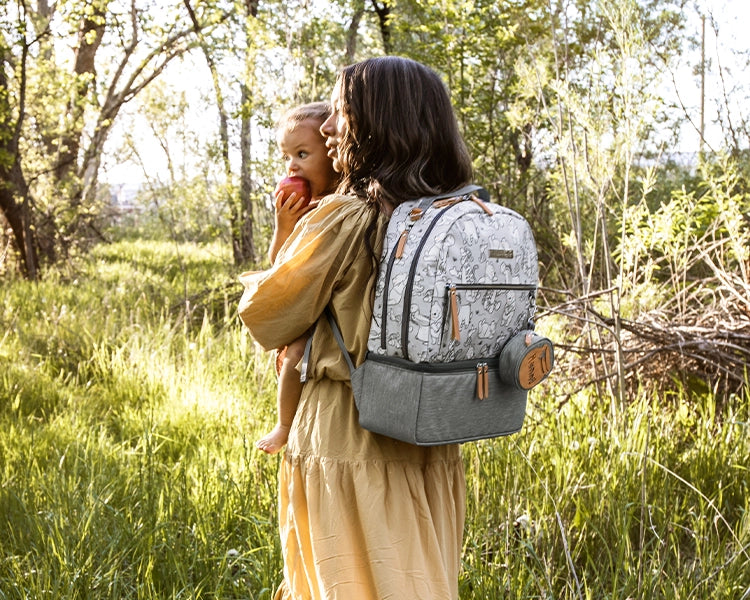 mom carrying baby girl while wearing the axis backpack in playful pooh