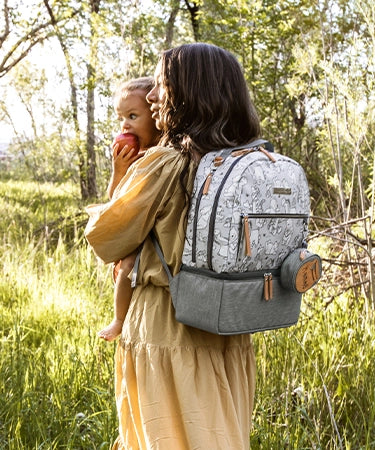 mom carrying baby girl while wearing the axis backpack in playful pooh