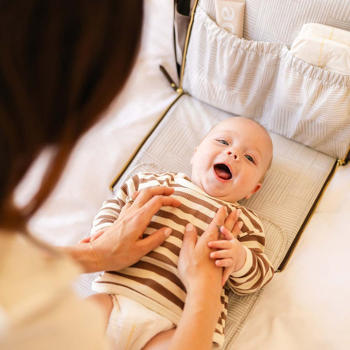 mom playing with baby while baby is lying on the diaper changing pad of the Boxy Backpack in Saddle