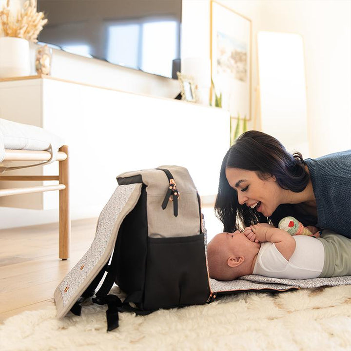mom playing with baby in front of boxy backpack in black/sand