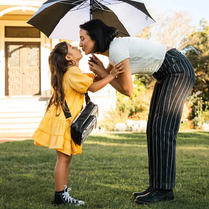 mom and baby girl kissing under an umbrella with baby girl wearing the Criss-Cross Sling in Halloween Town