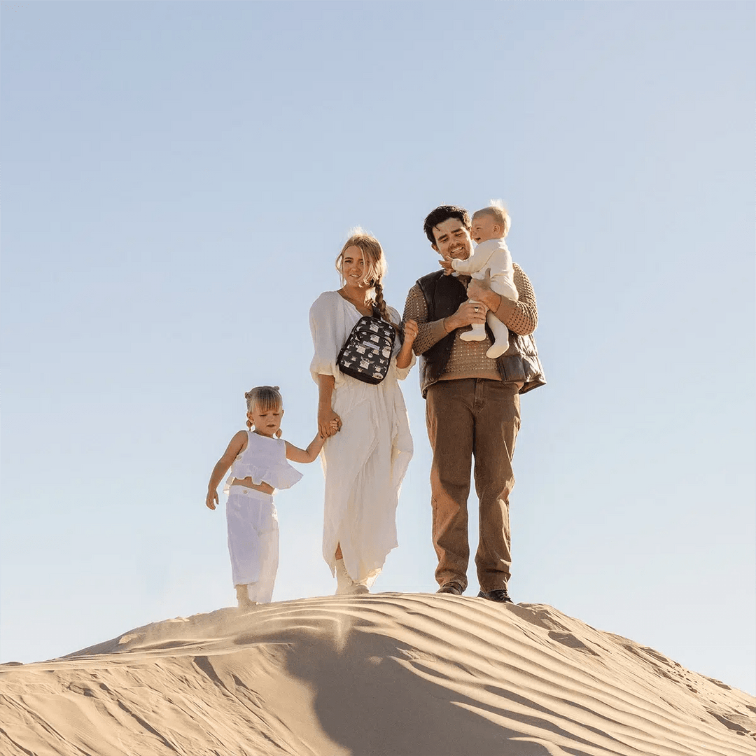 family picture of mom wearing the Criss-Cross Sling in The Child while holding hands with toddler girl and dad holding baby in arms