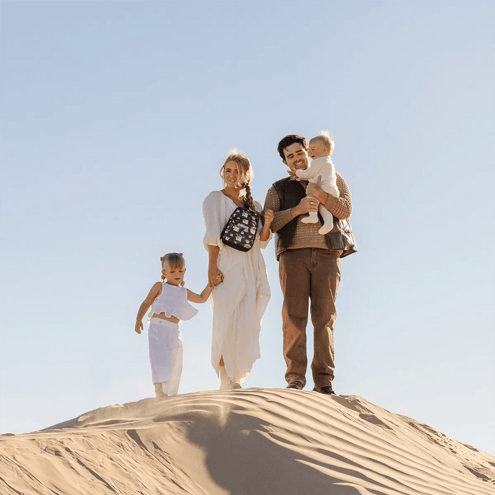 family picture of mom wearing the Criss-Cross Sling in The Child while holding hands with toddler girl and dad holding baby in arms