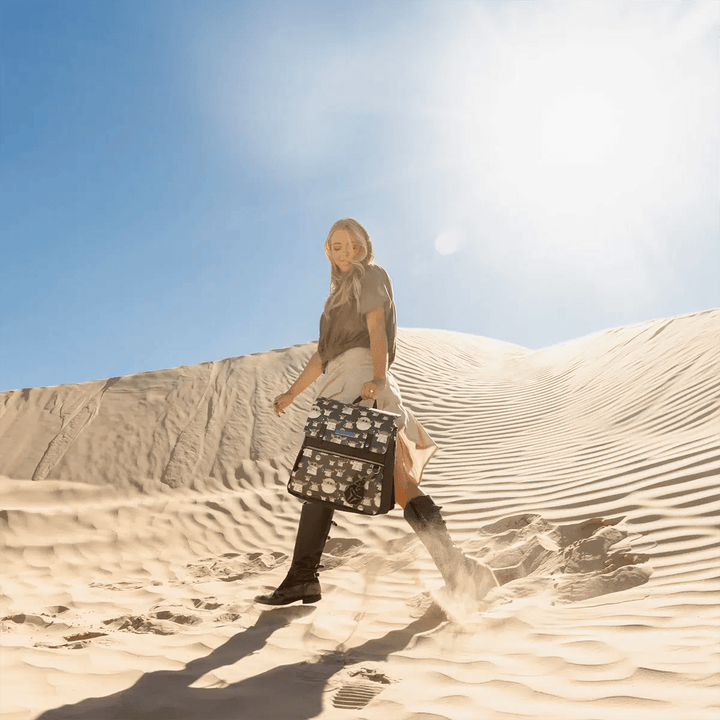 action shot of mom walking in desert sand while holding Meta Backpack in The Child