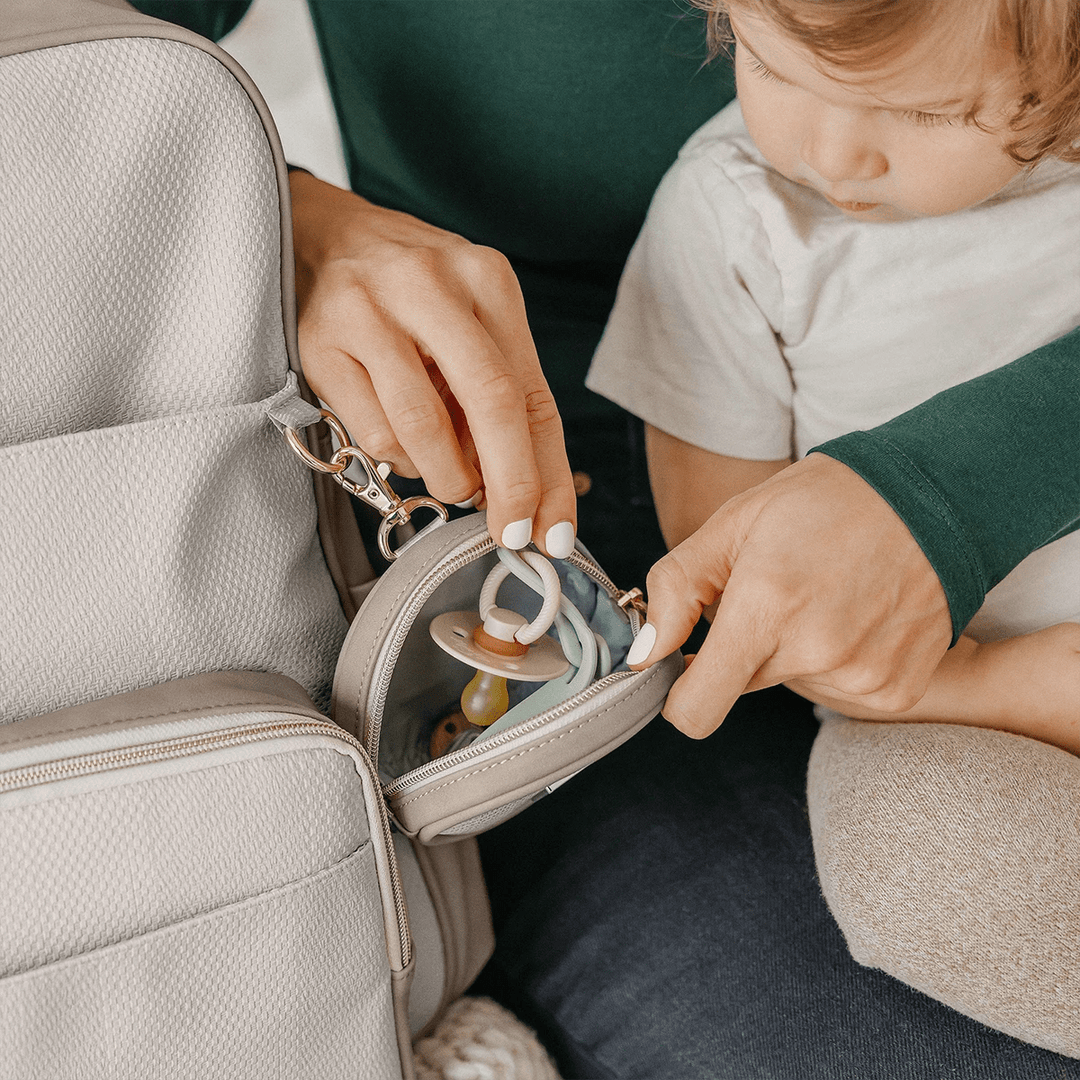 mom holding baby while putting inside pacifier inside the petite porter in grey matte cable stitch