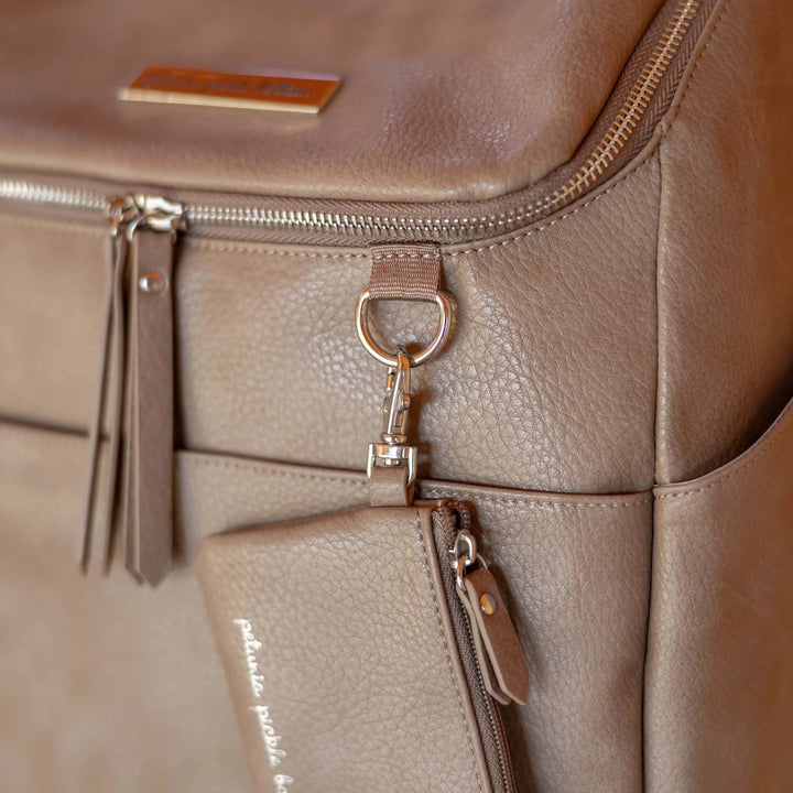 close up image of the d-ring and zippered pouch of the Tempo Backpack in Mink. A soft greige color with cool undertones