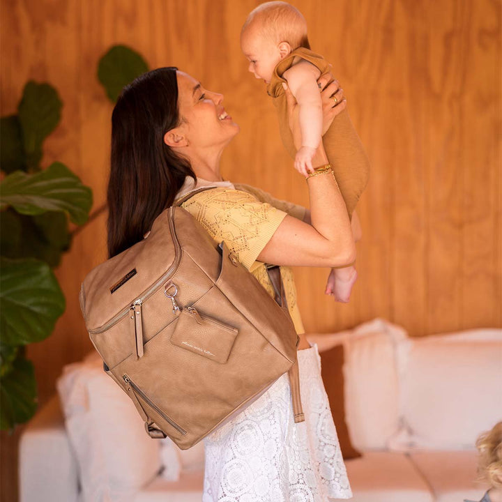 mom holding baby with Tempo Backpack in Mink over her shoulder