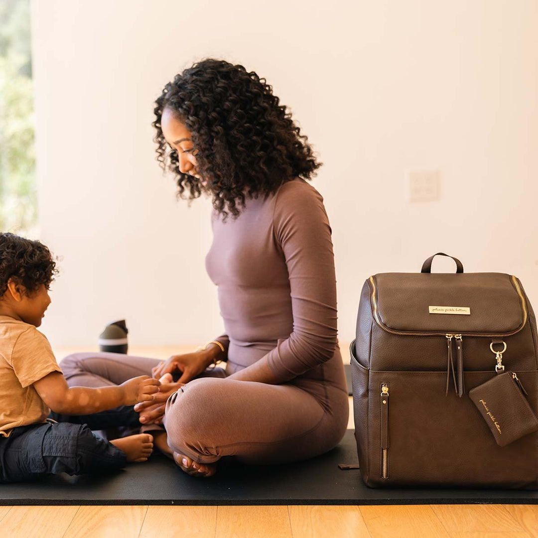 mom playing with kid on yoga mat next to the Tempo Backpack in Saddle